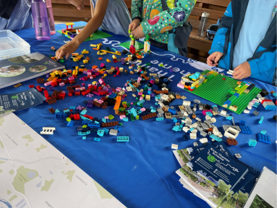 A table with a River Thames Scheme table cover that is covered in pieces of lego and children playing in the background