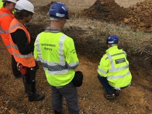 4 people standing in a hole, all wearing hi-vis and protective clothing. 