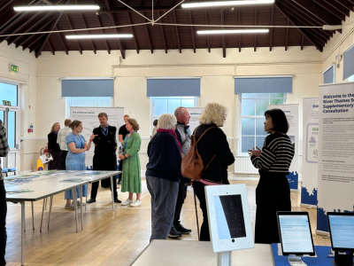 A group of people standing around some River Thames Scheme banners in conversation with the scheme specialists. 