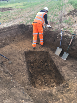 A person doing some archaeology surveys in a high-vis, hard hat and with some spades