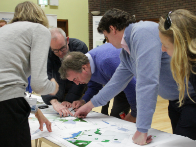 A group of 4 people in conversation at a table looking at the River Thames Scheme banners and consultation material.